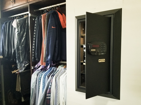 An open wall safe in a closet with clothing hanged.